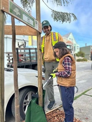 Kid watering newly planted tree with FUF staff member smiling and supporting.